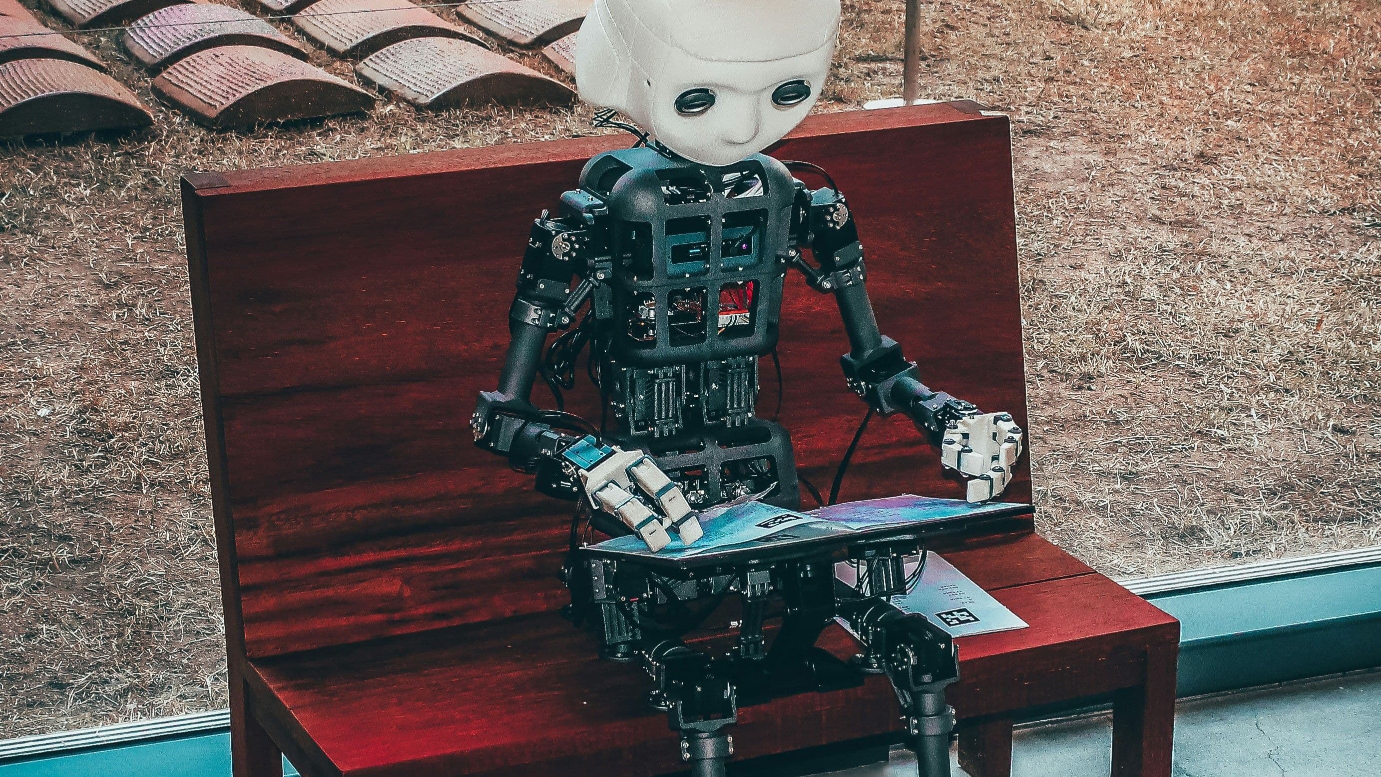 Humanoider Roboter sitzt auf einer Bank und hält ein Tablet.