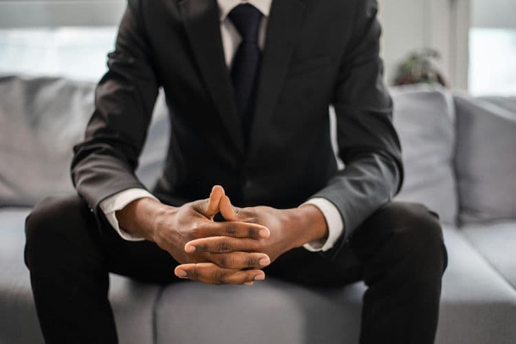 Symbolbild für Headhuinting: Frontalsicht auf einen Mann mit Businessanzug auf einem Sofa sitzend. Der Kopf ist nicht zu sehen.